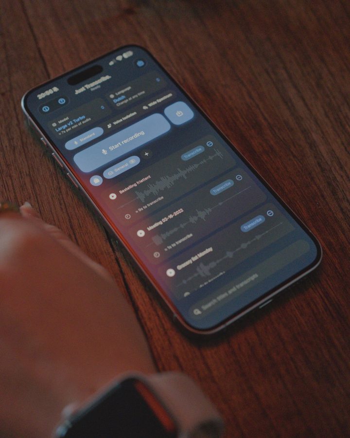 Een iPhone op een donkere houten tafel in de avond, met een lijst opnames in Just Transcribe.